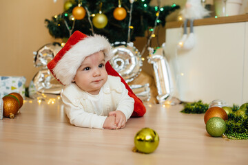 Cute smiling baby is lying under a festive Christmas tree and playing with gifts. Christmas and New Year celebrations