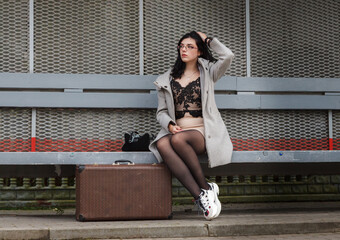 young girl in a gray coat with a suitcase sits on a bench at the railway station © Radnatt
