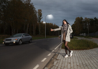 Fototapeta premium young girl in a gray coat stands near the road trying to stop a car