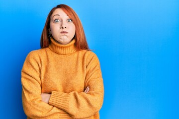 Beautiful redhead woman with arms crossed gesture puffing cheeks with funny face. mouth inflated with air, catching air.