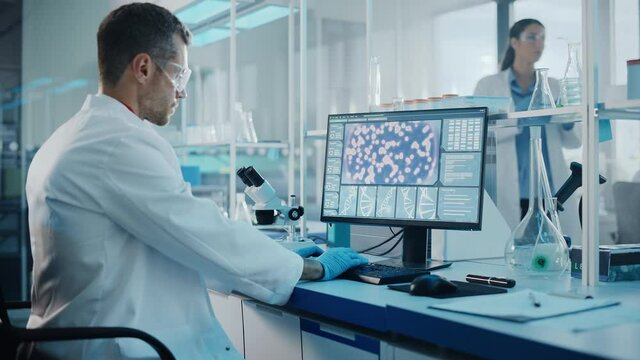 Medical Science Laboratory with Diverse Multi-Ethnic Team of Biotechnology Scientists Developing Drugs, Microbiologist Working on Computer with Display Showing Gene Editing Interface. Arc Dolly Shot