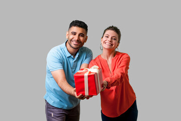 Please take your present! Young generous couple giving gift box to camera, looking with toothy...