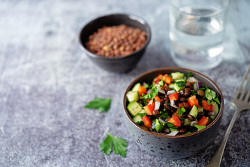 Green lentil red bell pepper cucumber parsley salad in a bowl