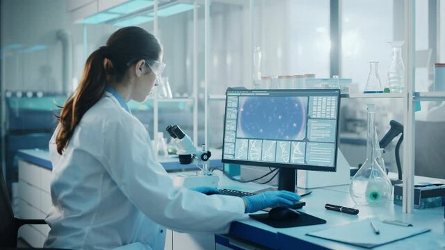 Medical Science Laboratory: Microbiologist Working on Computer with Display Showing Gene Editing Interface. Diverse Multi-Ethnic Team of Biotechnology Scientists Developing Drugs.Over Shoulder