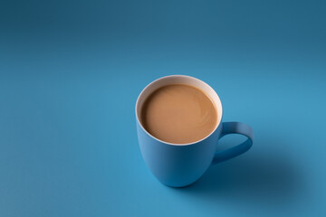 Cup of milk coffee on blue background, copy space for text