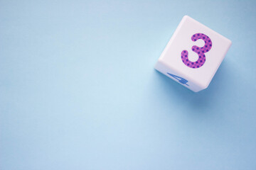 White plastic cube with a violet number 3 on a blue background in the upper right corner. With copy space