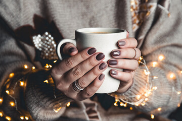A woman in warm clothes of neutral tones with a Christmas garland. matte stylish manicure - 399119562