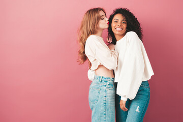 Two young beautiful smiling international hipster female in trendy summer jeans clothes. Sexy carefree women posing near pink wall in studio. Positive models having fun. Concept of friendship