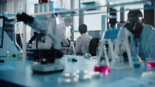 Medical Science Laboratory with Diverse Multi-Ethnic Team of Biotechnology Scientists Developing Drugs, Microbiologist Working on Computer with Display Showing Gene Editing Interface. Moving Shot