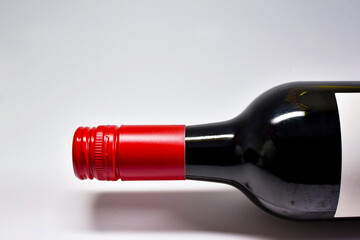 Close up of the top and neck of a screw cap bottle of red wine on a plain white background. No...