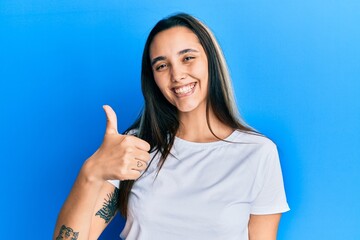 Young hispanic woman wearing casual white t shirt doing happy thumbs up gesture with hand. approving expression looking at the camera showing success.