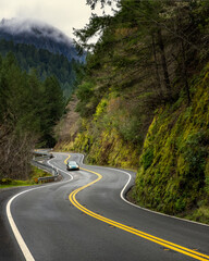 highway curving through mountain with trees, fog, car, moss
