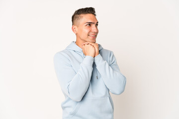 Young caucasian handsome man isolated keeps hands under chin, is looking happily aside.