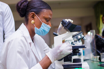 young african scientist looking through a microscope in the laboratory about the vaccine she is...