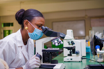 young african scientist looking through a microscope in the laboratory about the vaccine she is...