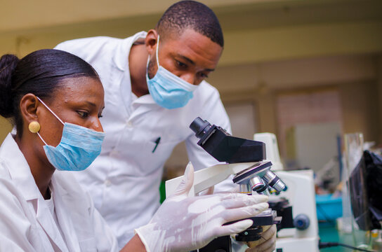 african health care researchers working in life science laboratory. young female research scientist and senior male supervisor preparing and analyzing microscope slides in the research lab