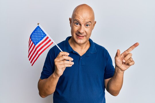 Middle age bald man holding united states flag smiling happy pointing with hand and finger to the side