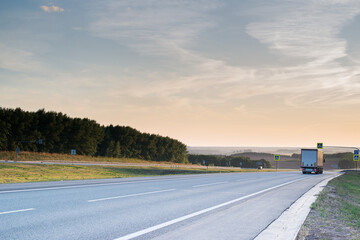 a cargo truck goes down a gray highway with a beautiful sunset in the sky and beautiful clouds in summer