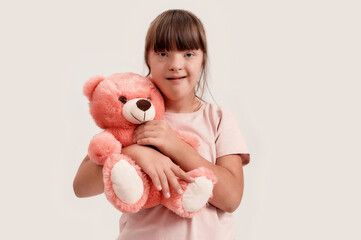 Portrait of disabled girl with Down syndrome looking at camera, holding her teddy bear while posing...
