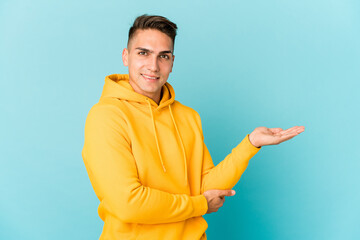 Young caucasian handsome man isolated showing a copy space on a palm and holding another hand on...