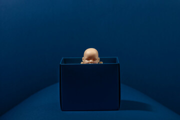 Baby doll in the dark blue box on blue background. Blue monday. Fear. Surprise.