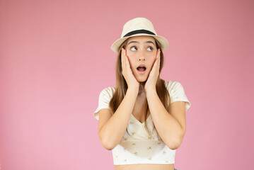 Surprised screaming woman in t-shirt and straw hat looking at the camera over pink background