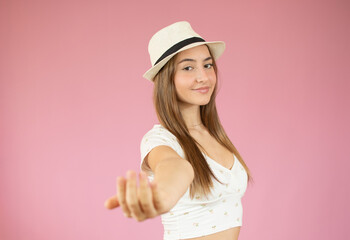 Young woman with straw hat over isolated pink background inviting to come with hand. Happy that you came