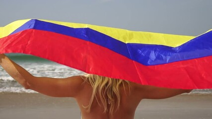 Young attractive woman with the flag of Colombia on the sea beach, slow motion