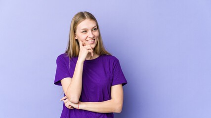 Young blonde woman isolated on purple background relaxed thinking about something looking at a copy space.