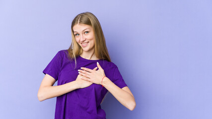 Young blonde woman isolated on purple background has friendly expression, pressing palm to chest. Love concept.