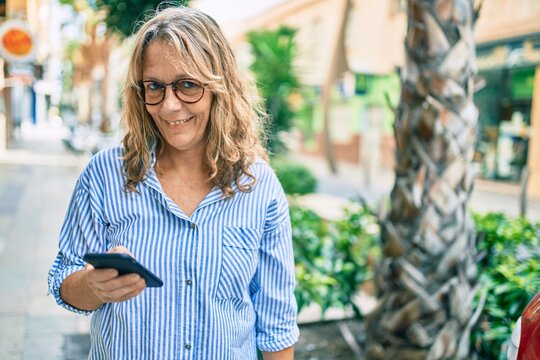 Middle age caucasian woman smiling happy using smartphone at the city.