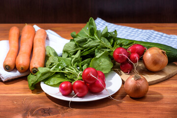 Fresh red radishes on wooden table with other vegetables. Growing organic vegetables. Large bunch of raw fresh juicy garden radish with onions, carrots and cucumber