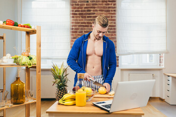 Male athlete, fitness trainer prepares fruit salad at home learns to cook online with laptop