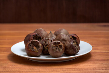 Fresh ripe organic common medlar fruit on a plate on wooden rustic background. Healthy food Mespilus germanica, top view