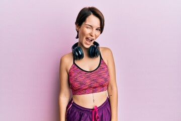 Young brunette woman with short hair wearing sportswear and headphones winking looking at the...
