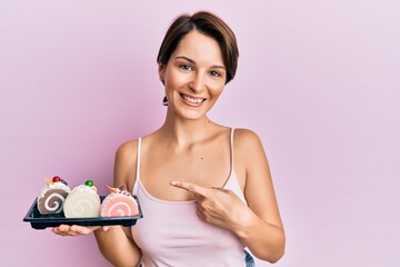 Obraz na płótnie Canvas Young brunette woman with short hair holding cake sweets smiling happy pointing with hand and finger