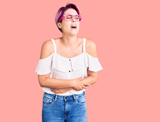 Young beautiful woman with pink hair wearing casual clothes and glasses with hand on stomach because nausea, painful disease feeling unwell. ache concept.