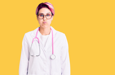 Young beautiful woman with pink hair wearing doctor uniform puffing cheeks with funny face. mouth inflated with air, crazy expression.