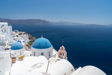 Famous Greek orthodox blue domed church and bell tower in Oia village on Santorini island, one of famous Greek Aegean Islands. Panoramic view from roof top