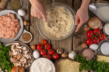Fototapeta premium Chef mix ingredients with spoon in glass bowl for cooking dough on wooden table with variety of ingredients background. Concept of cooking process. Backstage of preparing pie. View from above.