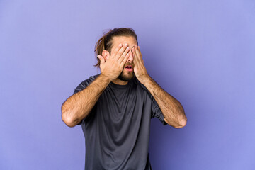 Young man with long hair look afraid covering eyes with hands.