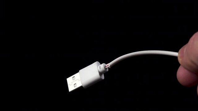 Damaged cable with USB plug. White broken phone charging cord in hand. Broken electronic device. Closeup on black background