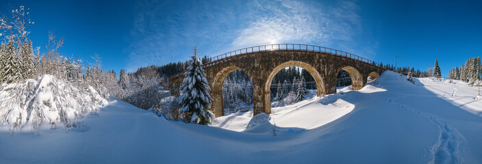 Stone viaduct (arch bridge) on railway through mountain snowy fir forest. Snow drifts  on wayside...