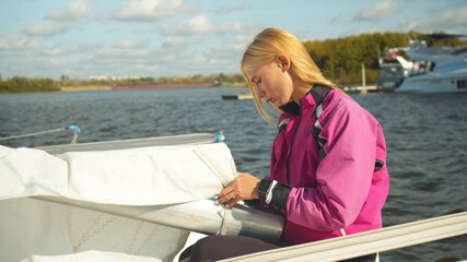 Fototapeta premium A pretty girl is preparing a white small yacht for a trip on the river on an autumn weekend
