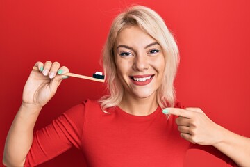 Young blonde girl holding toothbrush with toothpaste smiling happy pointing with hand and finger