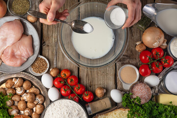 Chef hands pours some soda into glass bowl with milk for cooking dough on wooden table with variety of ingredients background. Concept of cooking process. Backstage of preparing pie. View from above.