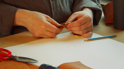 A young tailor's apprentice makes fasteners for a woman's bag and drinks coffee from a paper cup.