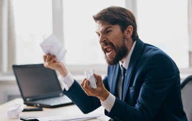 Fototapeta premium Aggressive business man in a suit with white sheets of paper in his hands in the office near the window