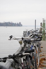 Parked bicycles at pier railings on Lake Constance in Germany in late autumn. Harbor pier in town Constance with bikes locked on the metal railings. A lake coast scene in vertical photo.