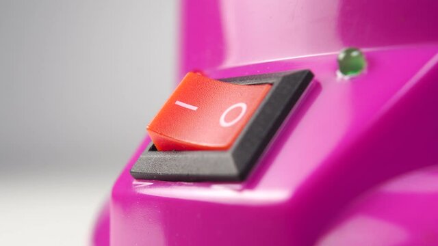 Pressing the red switch to the OFF position. Pink electrical appliance with a red button and a green LED. Macro shot. Close up. The idea of saving electricity and reducing utility bills